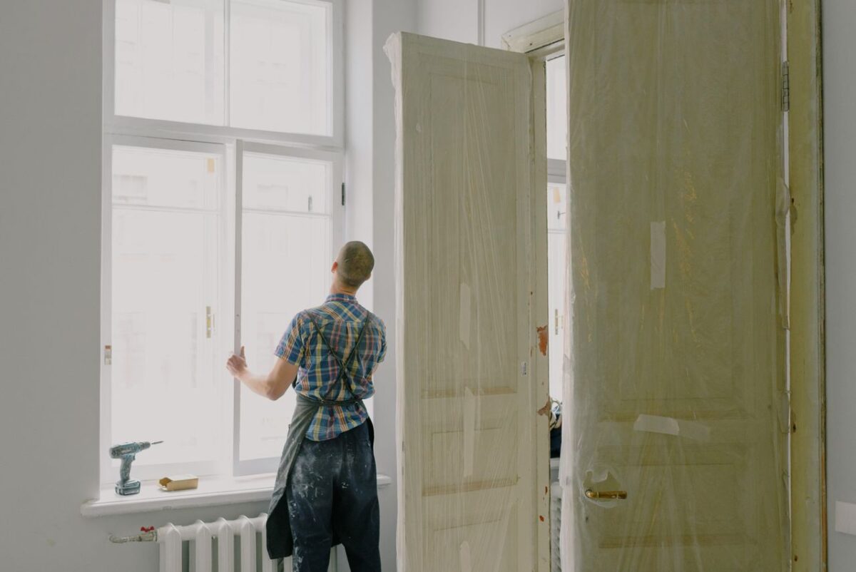 Services Back view of unrecognizable workman in apron mounting window near drilling machine and doors in flat